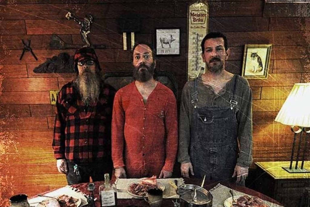 Integrantes da banda Macabre em ambiente rústico de madeira com mesa à frente e atmosfera sombria