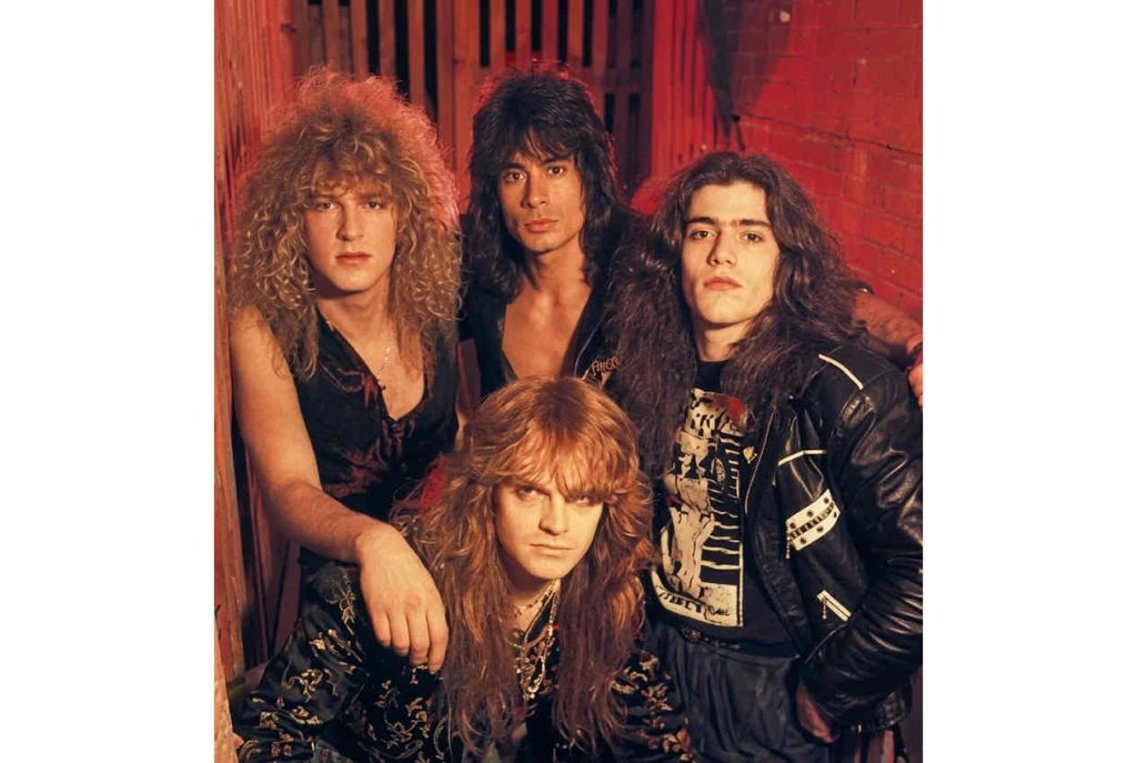 Retrato colorido da banda suíça Celtic Frost em 1987, com os integrantes Thomas Gabriel Fischer, Martin Eric Ain, Reed St. Mark e Ron Marks posando em um ambiente de luz avermelhada. Foto original por Lesley Evans.